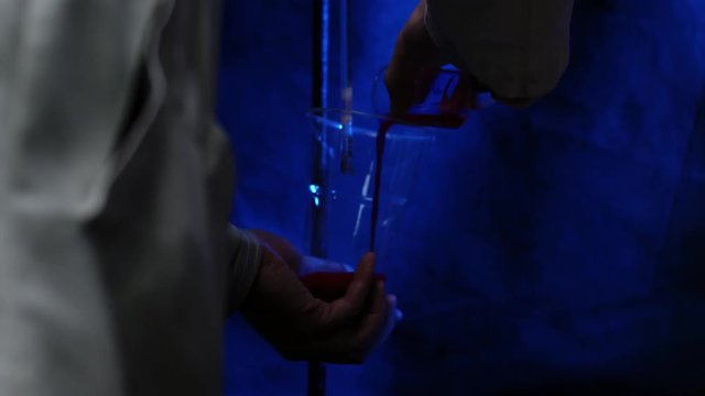 Chemist or medical research scientist adds chemicals to a flask for a violent chemical reaction