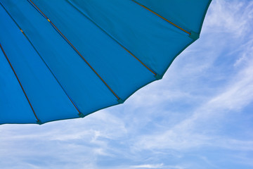 Fragment of a blue garden umbrella against the sky with 

clouds.
