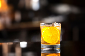 Closeup glass of godfather cocktail with slice of orange and ice cubes at bright bar background.