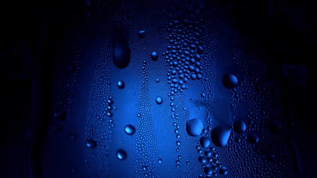 A drop of water on a glass close-up macro with sparkling bokeh on blue blurred background. Abstract drop water. Raindrop slide down the window glass, forming abstract figure