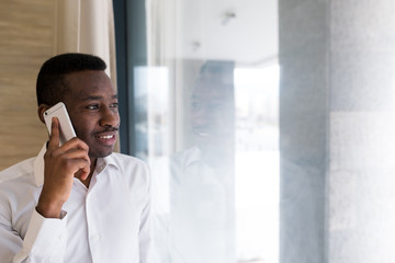 Young businessman checking his phone on an office. Bright photo of african man talking on his phone.