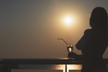 Silhouette of nude girl with cocktail in hands on sunset background