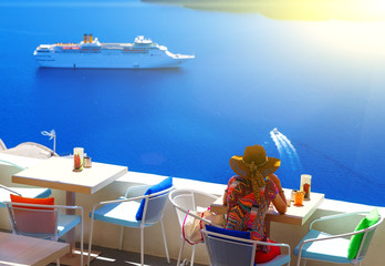 Woman in hat sitting in cafe and enjoys views of the Caldera and cruise ship, Santorini, Fira,...