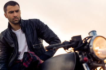 Handsome rider man with beard and mustache in black leather biker jacket sit on classic style cafe...