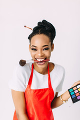 Beautiful young African American beautician woman holding set of make up brushes and eye-shadows