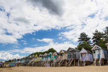 Rows of colourful wooden beach huts on a sandy beach in Norfolk, UK under a blue sky and summer sunshine.