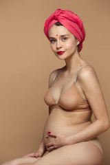 Young beautiful pregnant woman sitting on brown background