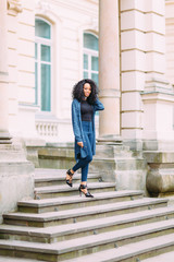 Young african american girl in jeans posing near old building