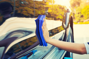 Asian woman's hand wiping surface of car by micro fiber cloth.