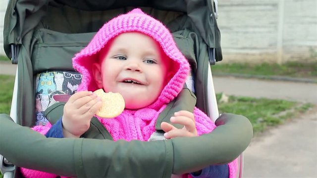 Baby girl sits in a baby stroller and eats an cookie