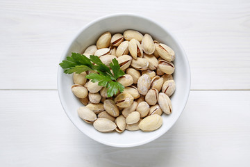 pistachio nuts in a bowl on white wooden background