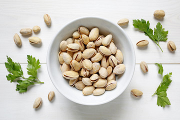pistachio nuts in a bowl on white wooden background