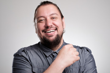 Portrait of laughing young man against grey wall. Happy guy smiling.