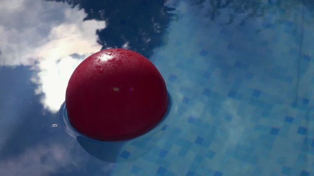Red ball floating in clear blue swimming pool water, plaything in poolside for summertime activity and recreation