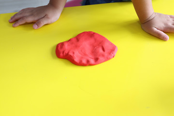 kid pressed red play dough on yellow table