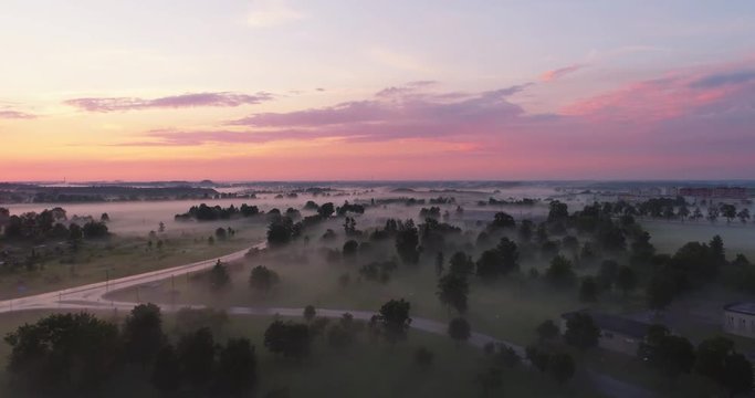 Aerial view flying over beautiful countryside fields through mysterious fog. Beautiful sunset.