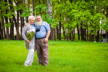 Naklejka na ściany i meble An elderly couple in love stands together in a park with flowers