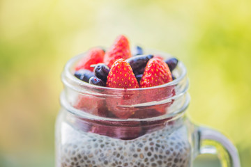 Healthy layered dessert with chia pudding, strawberry and honeysuckle in a mason jar on background...