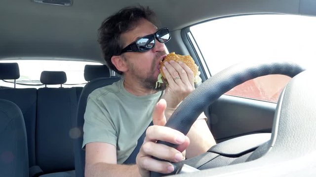 Man eating hamburger while driving car