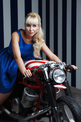 Obraz na płótnie Canvas Beautiful blonde in blue dress on a motorcycle in Studio