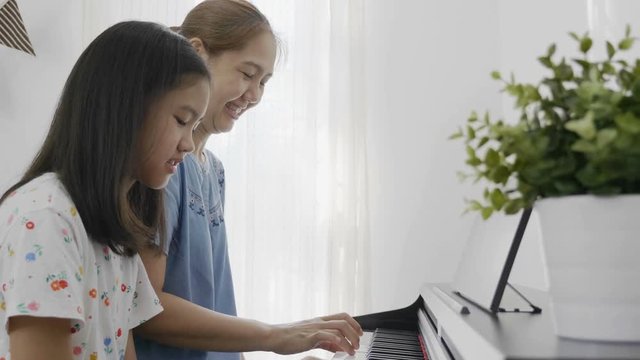 Slow motion of Asian girl playing piano with her mother, Zoom out shot