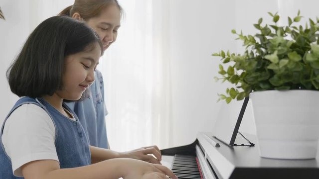 Slow motion of Asian girl playing piano with her mother, Zoom out shot