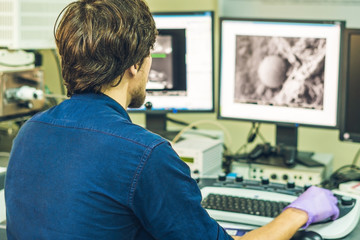 Scientist works at a electron microscope control pannel with two monitors in front of him