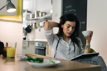 Online leisure time.young woman having coffee while working on her tablet at home