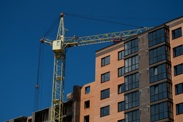 Crane and building construction.  New city place for many tall buildings under construction and cranes under a blue sky. Concrete building under construction. 