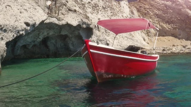 Red boat docked on an Island in front of a cave