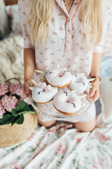 Girl in pajamas sits on a bed and holds a tray with donuts