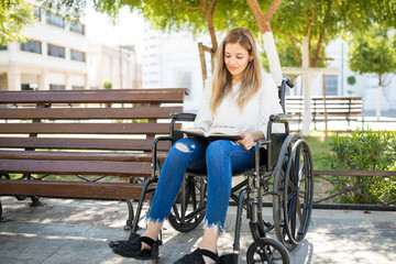 Fototapeta na wymiar Woman in wheelchair reading at a park