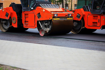 Two heavy compactor tires the upper layer of asphalt in the construction of a parking lot for...