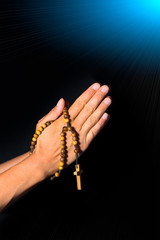 Praying Hands holding rosary beads on black background