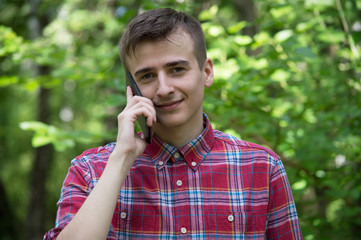 A guy smiles and talks on the phone in the park.