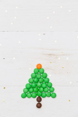 Top view on a small funny Christmas tree made of candies with golden stars confetti on white wooden background. Christmas and Happy New Year concept