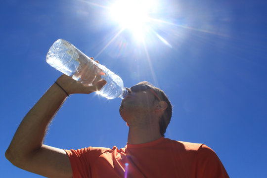 man drinking water with the sun over him