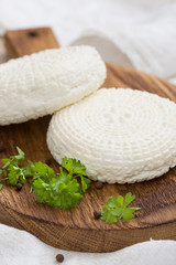 Closeup of round white homemade cheese - traditional milk creamy dairy product served with herbs on vintage wooden board. Rustic style.