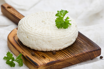 Closeup of round white homemade cheese - traditional milk creamy dairy product served with herbs on vintage wooden board. Rustic style.
