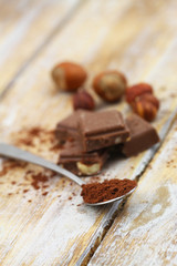 Cocoa powder on teaspoon and pieces on milk chocolate on rustic wooden surface
