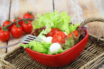 Mozzarella salad in red bowl on wooden surface
