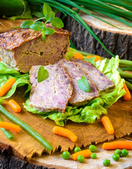 Meatloaf with peas, carrot, lettuce and herbs on a wooden board