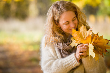 Portrait of young woman with maple leaves on autumn sunset background. Girl walking in the park and enjoying sunny weather. Lifestyle and autumn concept