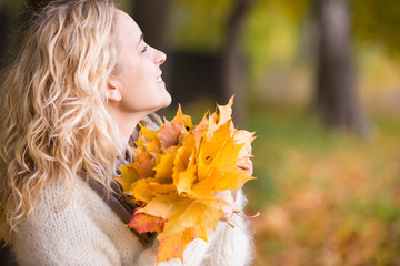Naklejka premium Portrait of young woman with maple leaves on autumn sunset background. Girl walking in the park and enjoying sunny weather. Lifestyle and autumn concept