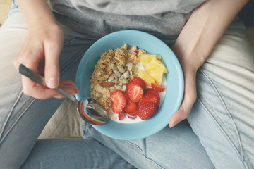 Eating healthy breakfast bowl. Yogurt, granola, seeds, fresh and dry fruits and honey in blue ceramic bowl in woman' s hands. Clean eating, dieting, detox, vegetarian food concept