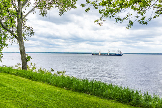 Cargo ship on Saint Lawrence river during summer with calm water and green grass
