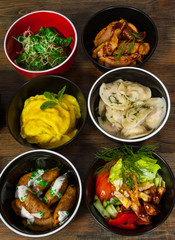 Set of different salad, dumplings and ravioli on a wooden table