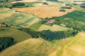 Aerial view of rural landscape. Small village with pond in middle of field in summer