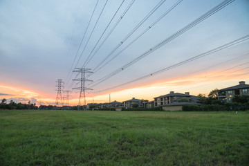 Group silhouette transmission towers (steel lattice/power tower, electricity pylon) next to apartment complex at sunset in US. Texture high voltage pillar, overhead power line, industrial background.