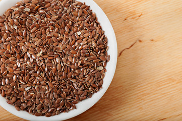 Flax seeds on a white plate, on an old wooden background, top view.